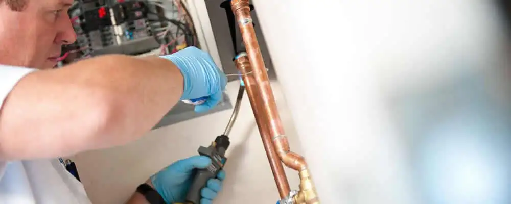 Water heater repair technician testing copper pipe connections and controls in Wilmington, NC
